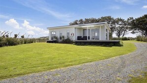 A modern house with a covered porch, a well-maintained lawn, and a gravel driveway. - Surfs up beach Bach  (Colac Bay)