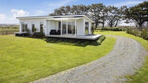 A modern house with a covered porch, a gravel driveway, and a well-maintained lawn. - Surfs up beach Bach  (Colac Bay)
