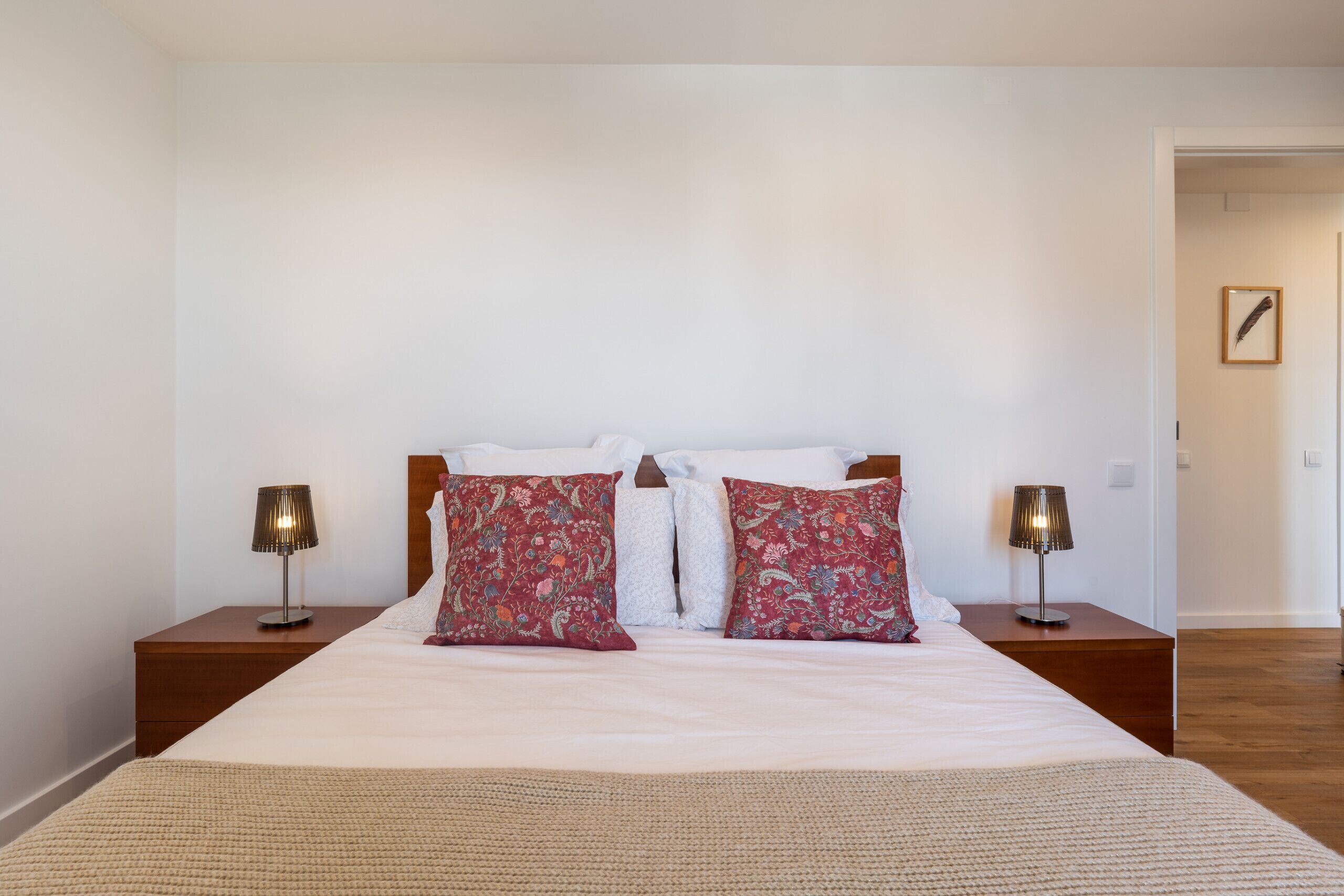 A neatly made bed with white and patterned pillows, two bedside lamps, and a framed picture on the wall.