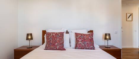 A neatly made bed with white and patterned pillows, two bedside lamps, and a framed picture on the wall.