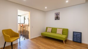 Ein Zimmer mit einem grünen Sofa, einem gelben Sessel, Holzboden und einer gerahmten Seekarte an der Wand.