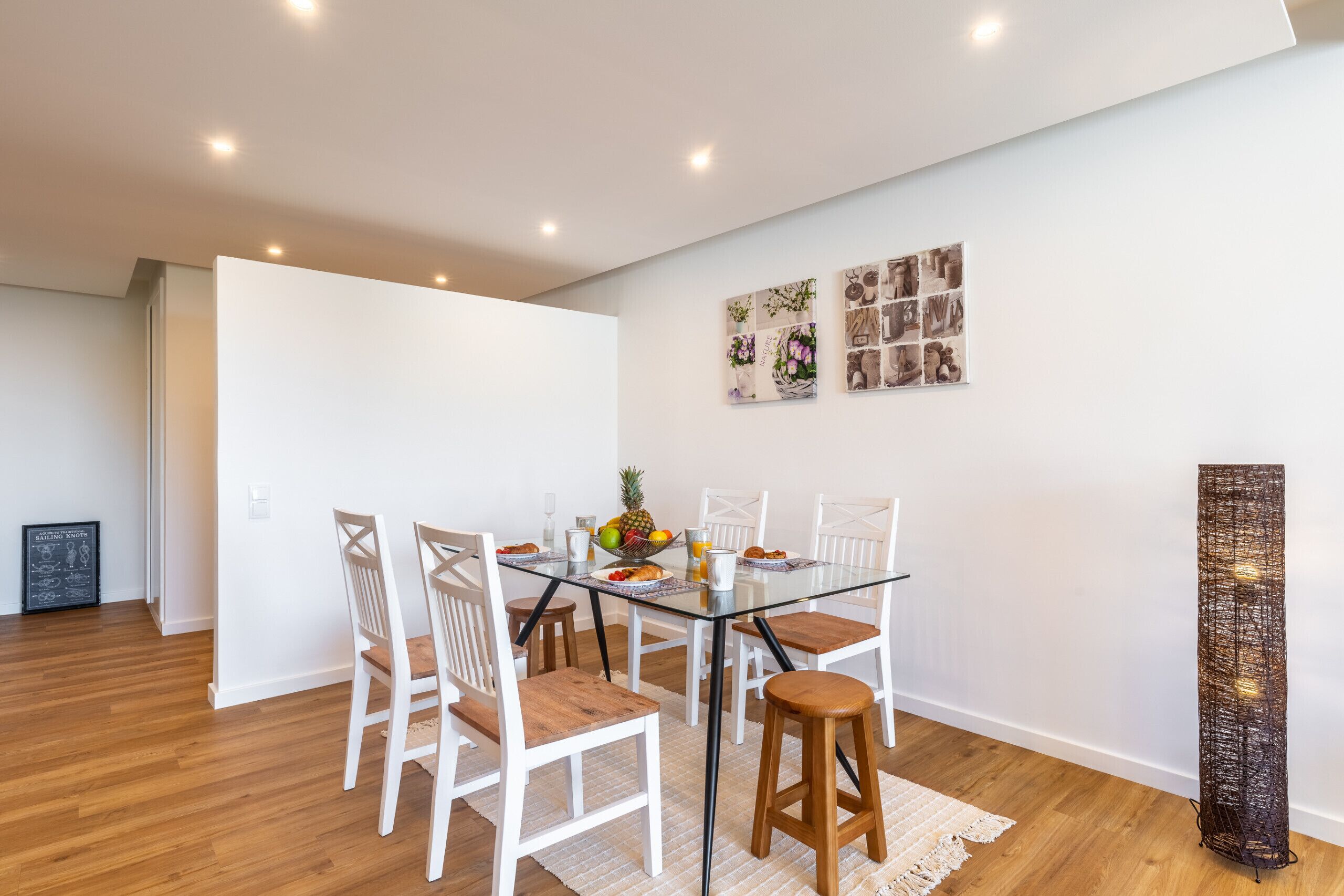 A dining area with a glass table, white chairs, and a woven floor lamp.