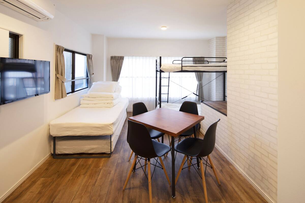 Une chambre compacte comprenant un lit superposé, un téléviseur à écran plat, une petite table à manger avec des chaises et un canapé.