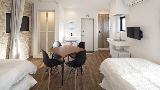 A hotel room with two beds, a wooden dining table with chairs, a small kitchenette, a TV mounted on the wall, and a window with curtains. - Hotel Little Bird Oku-asakusa (Tokyo)