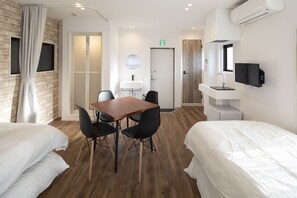 A hotel room with two beds, a wooden dining table with chairs, a small kitchenette, a TV mounted on the wall, and a window with curtains. - Hotel Little Bird Oku-asakusa (Tokyo)