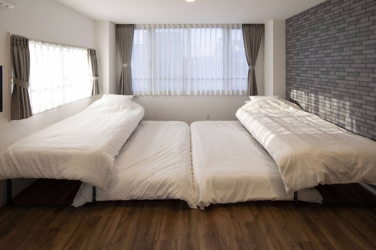 Une chambre avec deux lits simples, une fenêtre avec des rideaux, un mur en briques et un plancher en bois.
