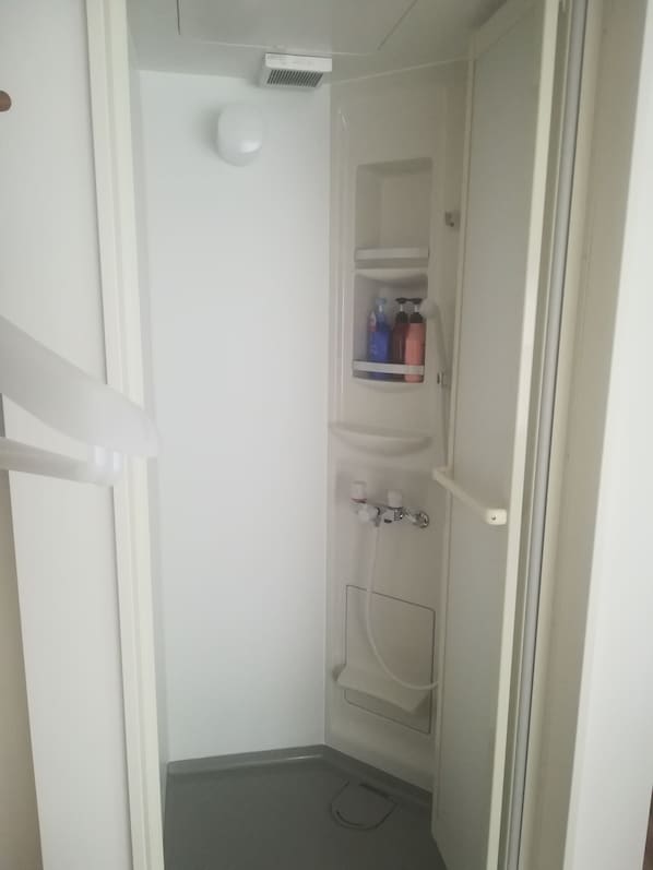 A small, white bathroom with a shower, a toilet, and a shelf with toiletries. - Hotel Little Bird Oku-asakusa (Tokyo)