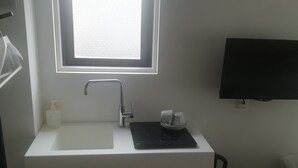 A small, modern bathroom with a white sink, a window above the sink, a black electric kettle, and a white storage box. - Hotel Little Bird Oku-asakusa (Tokyo)