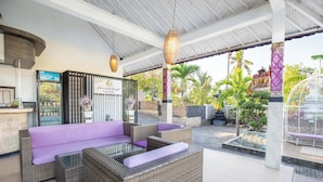A covered outdoor seating area with wicker furniture and purple cushions, a refrigerator, and a decorative wall with a sign. - Akusara Jungle Resort And Spa (Penida Island)