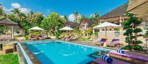 A pool area with lounge chairs and umbrellas, surrounded by buildings with a tropical architectural style. - Akusara Jungle Resort And Spa (Penida Island)