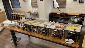 A buffet setup with various food items in trays, a coffee machine, and seating arrangements.