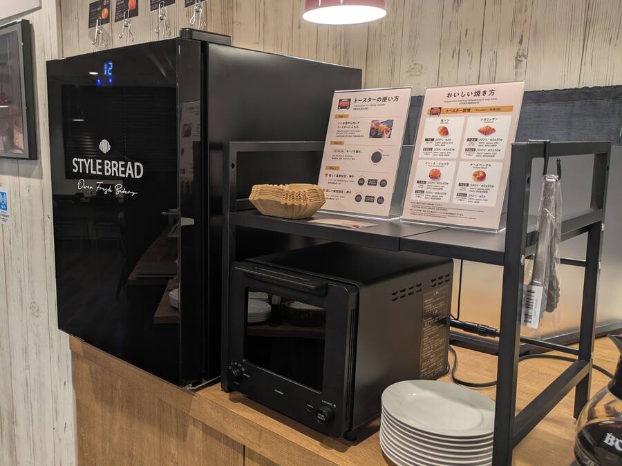 A toaster oven with a display and instructions, a bowl of bread, and a stack of plates on a wooden counter.