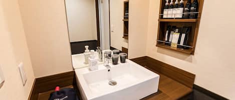 Een hotelbadkamer met een wit wastafel, een spiegel en een plank met toiletartikelen.