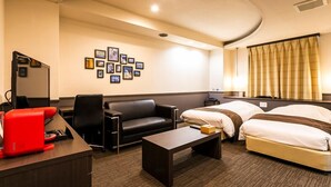 Habitación de hotel con sofá, dos camas individuales, escritorio con cafetera roja, una mesita y una pared decorada con cuadros.