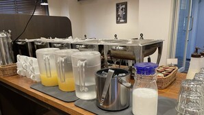 Montaje tipo bufé con vasos de vidrio transparente, jarras de bebidas y diversos alimentos sobre una barra de madera.