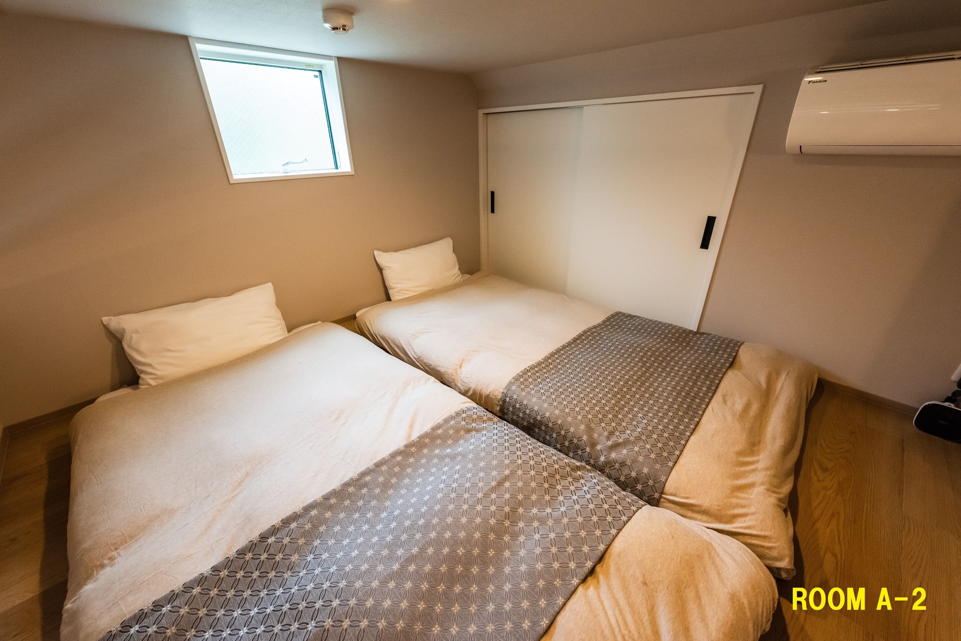 Ein Zimmer mit zwei Betten, einem Fenster, einer Klimaanlage und einer Tür.