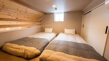 A bedroom with two beds, wooden slats on the ceiling, a small window, and a door.