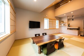 Una habitación tradicional japonesa con suelo de tatami, una mesa de madera para comer y un televisor montado en la pared.