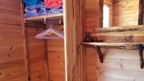 A wooden room with a corner wardrobe containing folded clothes and a hanging rack. - Minnow cabins, peaceful bush setting, cabin 2 (Lower Beulah)