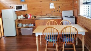 A wooden cabin kitchen with a refrigerator, microwave, stove, and wooden dining table with chairs. - Minnow cabins, peaceful bush setting, cabin 2 (Lower Beulah)