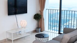 Una sala de estar moderna con un televisor de pantalla plana montado en la pared, una mesa de centro de vidrio, un sofá gris y vistas de la ciudad a través de amplias ventanas.