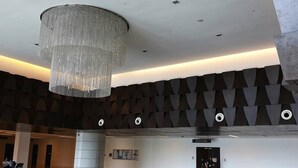 Un vestíbulo amplio con un candelabro moderno, suelo con diseño y un diseño geométrico en la pared.
