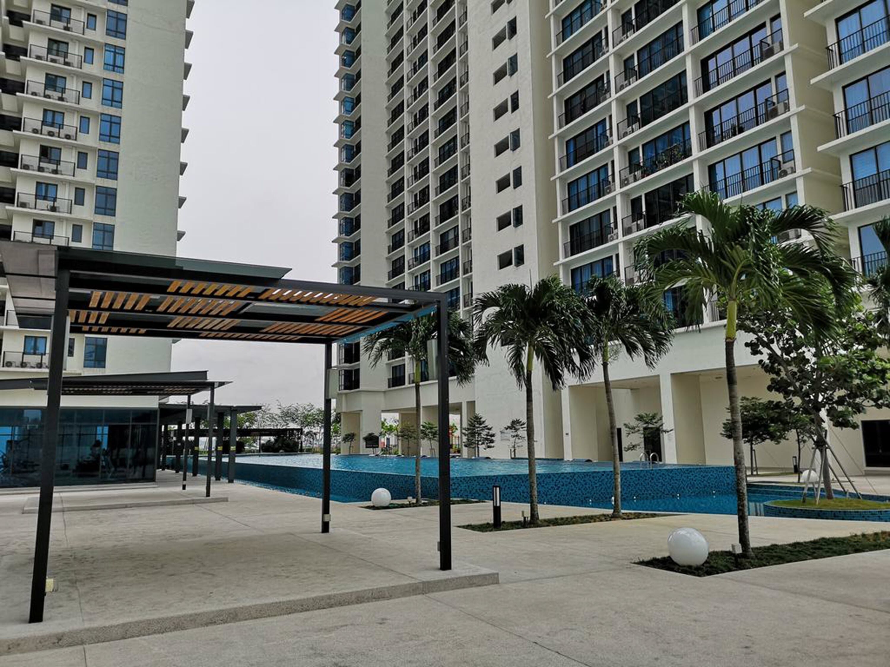 A modern residential building with a covered outdoor area, palm trees, and a swimming pool.