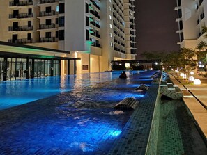 A swimming pool with a water feature, surrounded by a building with multiple floors and balconies. - Machome GuestHome at Trefoil Setia City (Shah Alam)