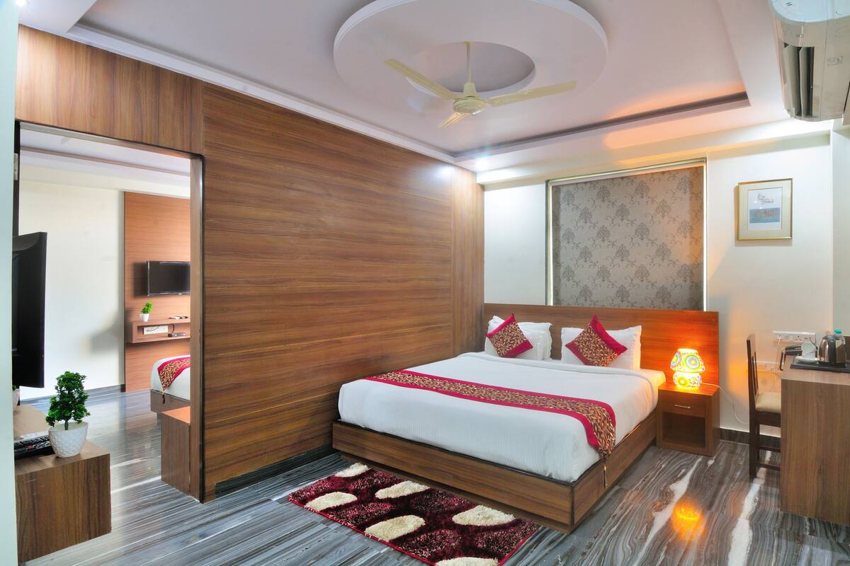 A modern bedroom with a wooden headboard, a large bed with white bedding and red accents, a bedside table with a lamp, and a ceiling fan.