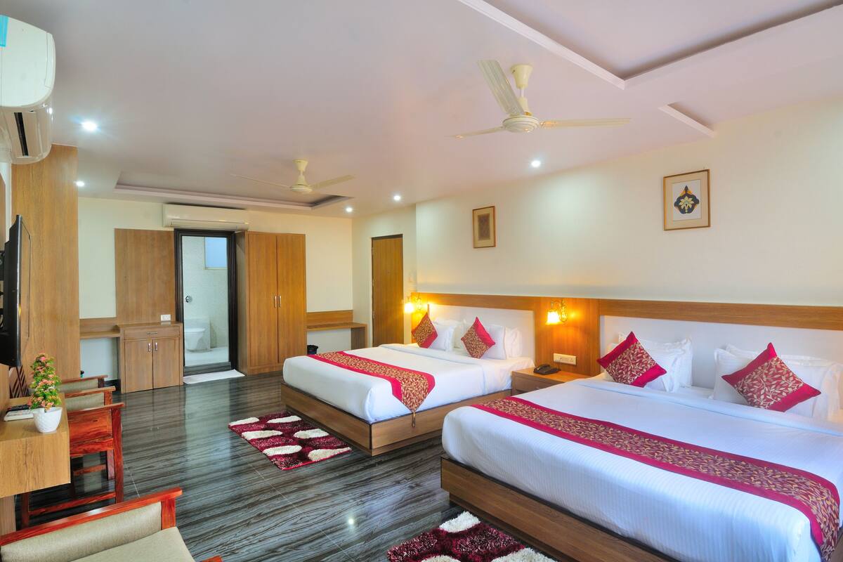 A hotel room with two beds, wooden furniture, a desk, and a ceiling fan.