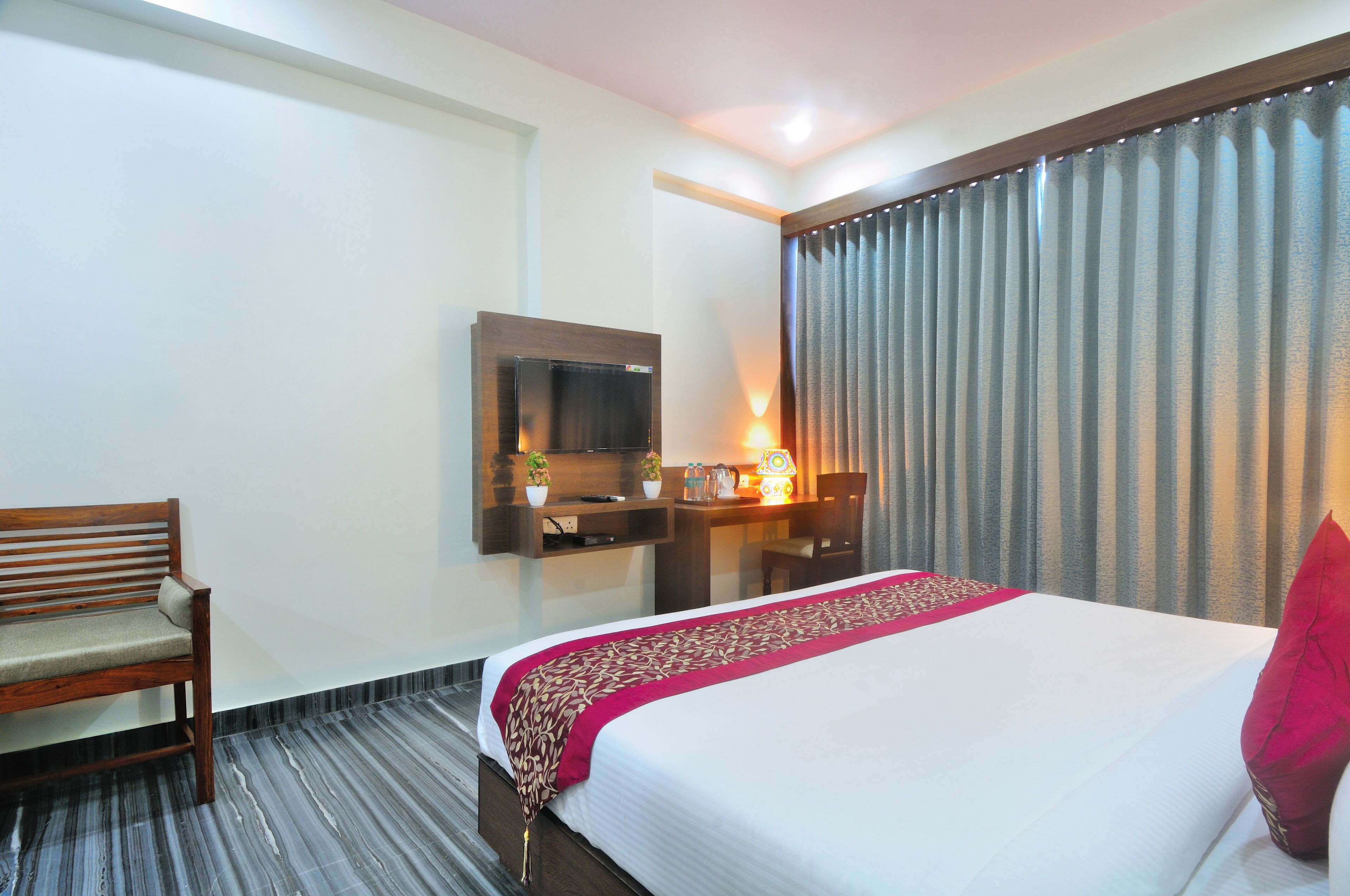 A hotel room with a bed, a desk, a chair, a TV, and a window with curtains.