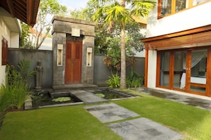Experience a serene courtyard with a well-maintained lawn and a small water feature, surrounded by lush greenery and a tall palm tree.