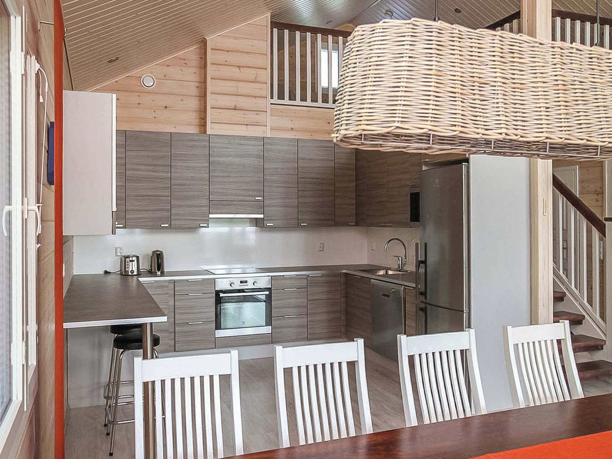 Une cuisine moderne dotée d’appareils électroménagers en acier inoxydable, d’un îlot central et d’un luminaire suspendu en osier.