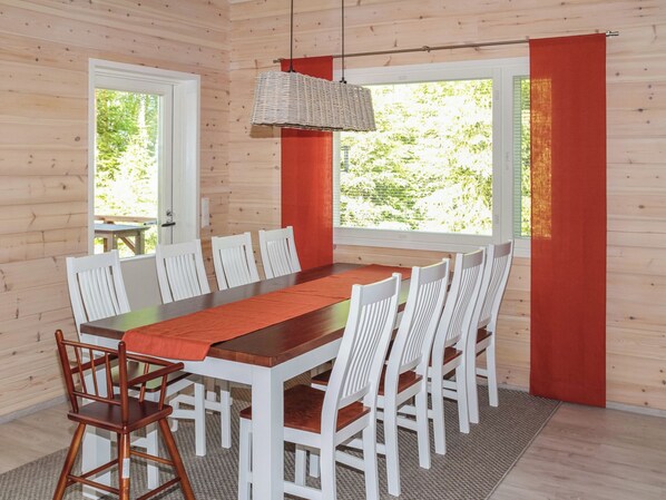 Zona pranzo con tavolo e sedie in legno, lampada a sospensione intrecciata e ampie finestre con tende.