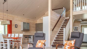 A spacious living area with a high ceiling, a staircase, and a dining area with chairs and a table.