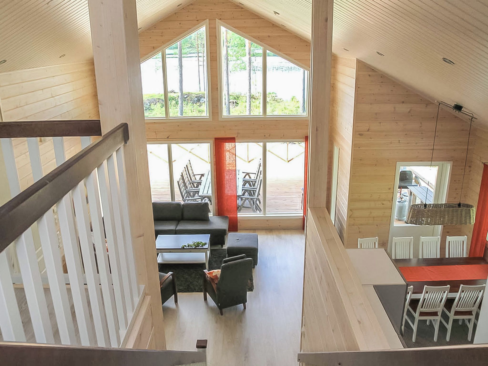 A spacious loft-style room with a high ceiling, large windows, a seating area with a sofa and chairs, and a dining area with a table and chairs.