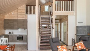 Amplia sala de estar con techo alto, paredes de madera, una escalera, una cocina con electrodomésticos modernos y una chimenea.