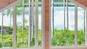 Una cabaña con amplios ventanales que ofrecen vistas a un lago y un bosque.