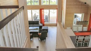 Amplia habitación estilo loft con techo alto, ventanas grandes, una escalera, una zona de estar con sofá y sillas, y un comedor con mesa y sillas.
