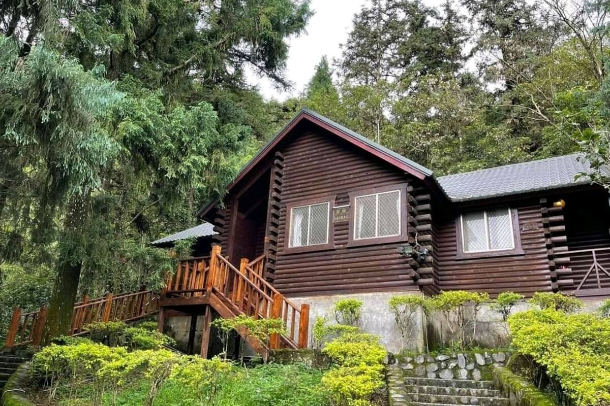 Eine Blockhütte mit einer Holztreppe, die zu einer Veranda führt, umgeben von üppiger Vegetation und Bäumen.