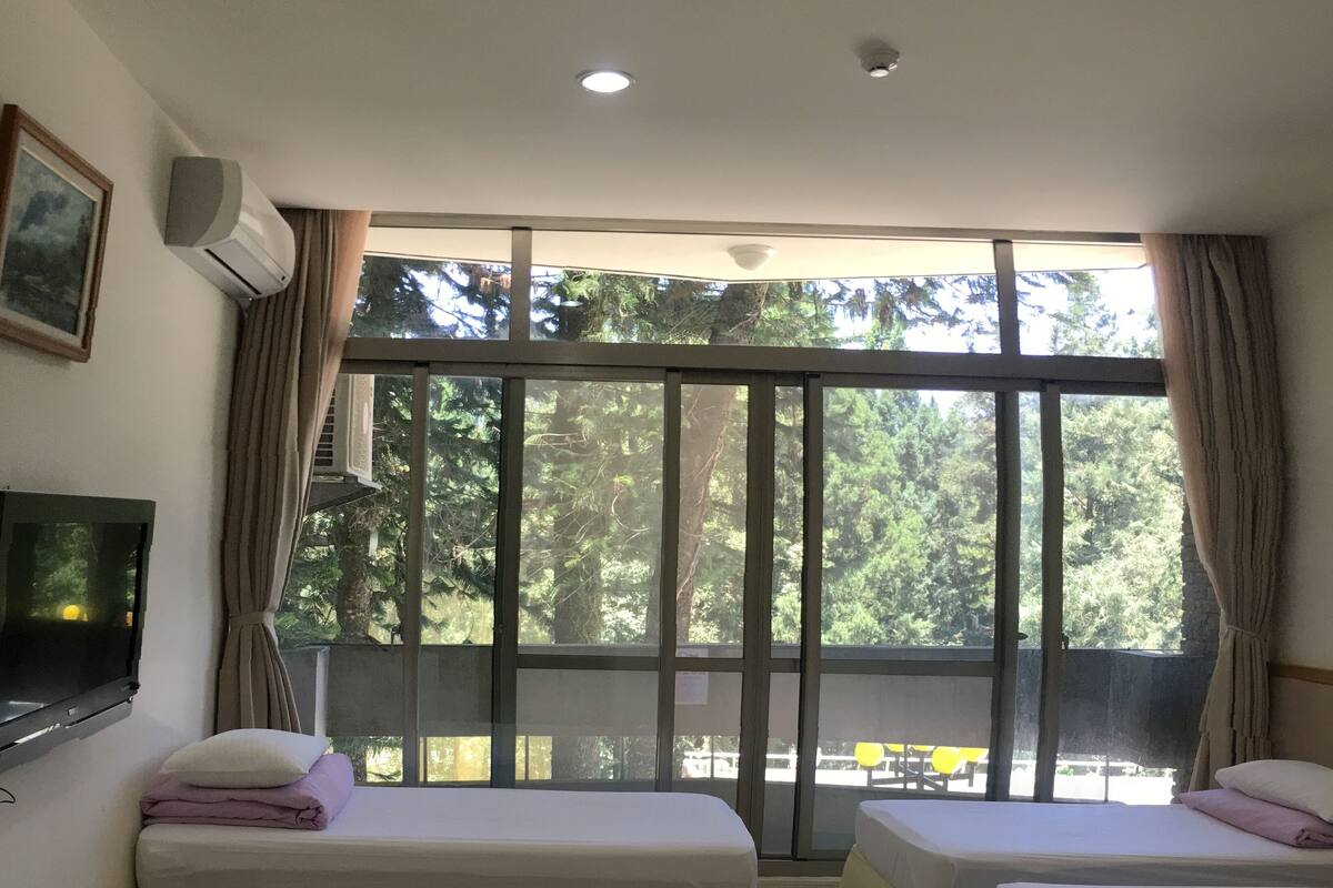 Ein Zimmer mit zwei Betten, einem Fernseher und einem großen Fenster mit Vorhängen.
