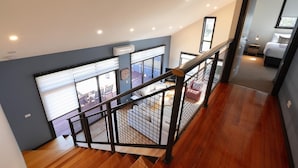 A modern interior with a wooden staircase, a balcony with outdoor furniture, and a bedroom with a bed and nightstand. - Cove View Retreat (St Helens)