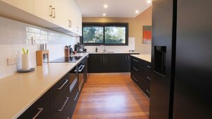 A modern kitchen with black cabinets, a stainless steel refrigerator, and a window providing natural light. - Cove View Retreat (St Helens)