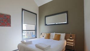 A hotel room with a large bed, a bedside table with a lamp, and a window with a view of the outside. - Cove View Retreat (St Helens)