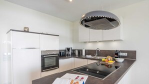 A modern kitchen with white cabinets, a central island, and a built-in stove. - Terrace apartment Haffblick - Oasis on the lagoon - Haffblick (6-2) (Garz)