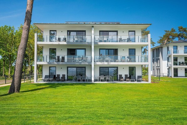 A modern multi-story residential building with balconies, large windows, and a well-maintained lawn.