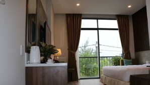 A hotel room with a large bed, a desk with a lamp, a potted plant, and a view of greenery through the window. - ENTIRE VILLA#11BEDROOMS#ROOFTOPPOOL#danangbayview (Đà Nẵng)