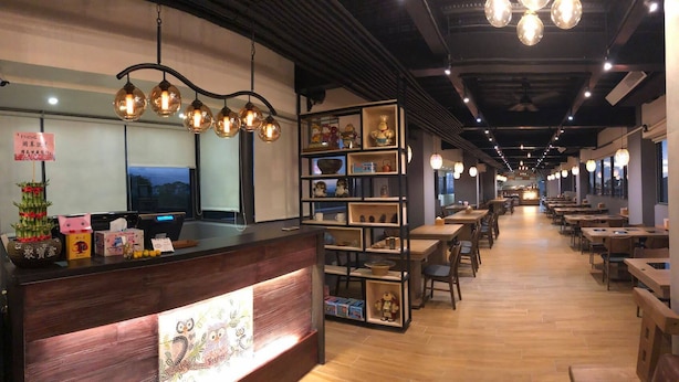 L’intérieur d’un restaurant est aménagé avec des tables et des chaises en bois, un comptoir où sont exposés divers articles, et des luminaires sphériques suspendus au plafond.