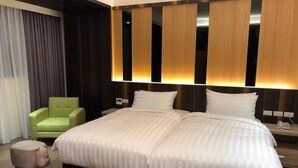 Une chambre d’hôtel avec un grand lit, un fauteuil vert et un petit pouf.