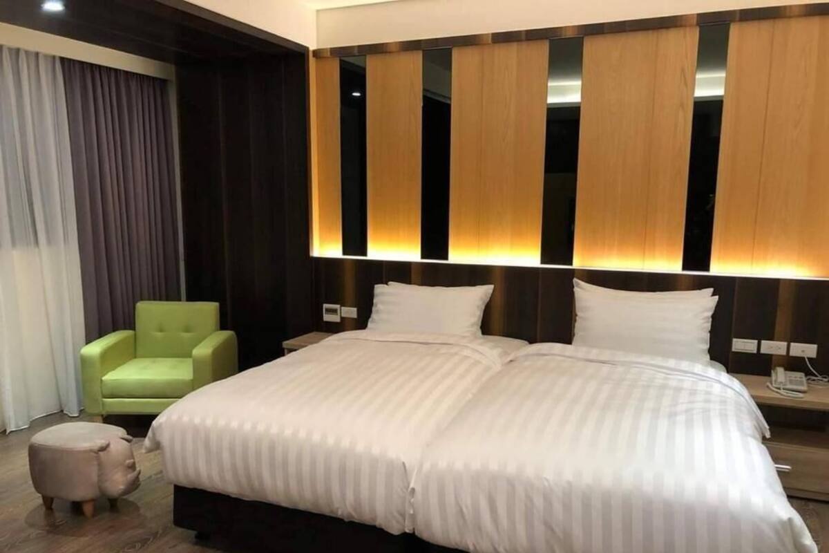 Une chambre d’hôtel avec un grand lit, un fauteuil vert et un petit pouf.